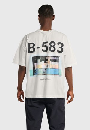 Witte oversized T-shirt met een grafisch ontwerp met "B-583" en een patroon van kleurrijke rechthoeken op de achtergrond, gemaakt van katoen.