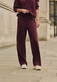 Hanorac bordo și pantaloni cu picioare largi din material moale, cu croială relaxată și detalii subtile de cusături, asortați cu adidași albi.