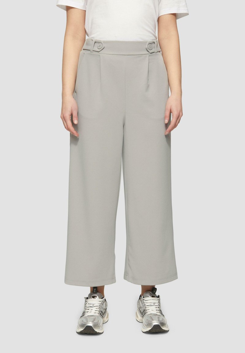 Hellgraue weite Hose mit hoher Taille, ausgestattet mit zwei Knopfakzenten und Falten. Kombiniert mit silbernen Sport-Sneakern.