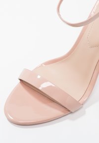 Nude lakované kožené sandály na vysokém podpatku s širokým předním páskem a elegantní špičatou špičkou. Hladký povrch s lesklým finišem.