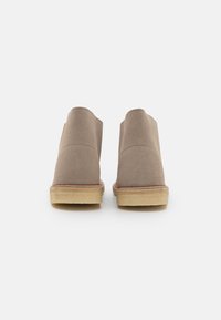 Beige suede ankle boots with a smooth texture, low heel, and visible stitching along the sole, featuring a rounded toe and minimal design.