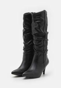 Black knee-high boots made of smooth faux leather with a slouchy design, pointed toe, and a 3-inch heel. Zipper closure on the side.