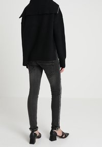 Suéter negro acanalado con cuello doblado, combinado con jeans ajustados grises con una franja plateada en el lateral y dobladillo desgastado. Zapatos negros de tacón bloque.