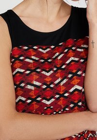 Robe à motifs rouge et noir avec un design géométrique comportant des lignes horizontales et diagonales. Le haut présente un col noir uni.