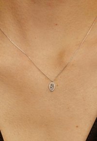Collar de plata esterlina con un colgante ovalado adornado con piedras preciosas transparentes, que presenta una cadena delicada y un diseño minimalista.