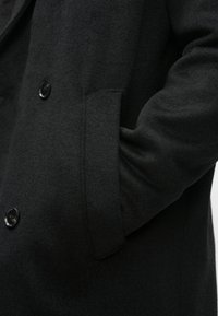 Sort uldfrakke med dobbeltradet design, glat tekstur, store knapper og sidelommer. Skræddersyet pasform med strukturerede skuldre.