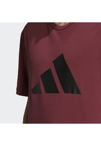 Bordeaux bomulds T-shirt med et stort sort geometrisk logo på tværs af brystet; rund halsudskæring og korte ærmer. Blød tekstur.