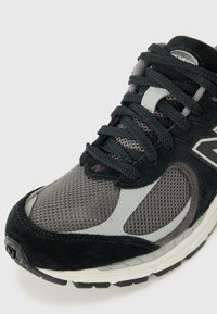 Chaussure de sport noire et grise avec une tige en maille, des accents en daim, une languette rembourrée, des lacets texturés et une semelle en caoutchouc avec des crampons.