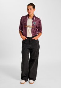 Koszulka polo w bordowo-kremowe paski z kołnierzykiem, stylizowana z czarnymi dżinsami o wysokim stanie i kremowymi trampkami. Wyraźne logo graficzne.