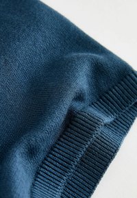 Gros plan d’un tissu tricoté bleu foncé montrant une texture détaillée et un ourlet côtelé sur un fond clair.