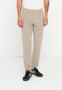 Chinos beige en coton avec des jambes droites, dotés de poches avant, d'une fermeture à bouton, portés avec des chaussures de sport noires.