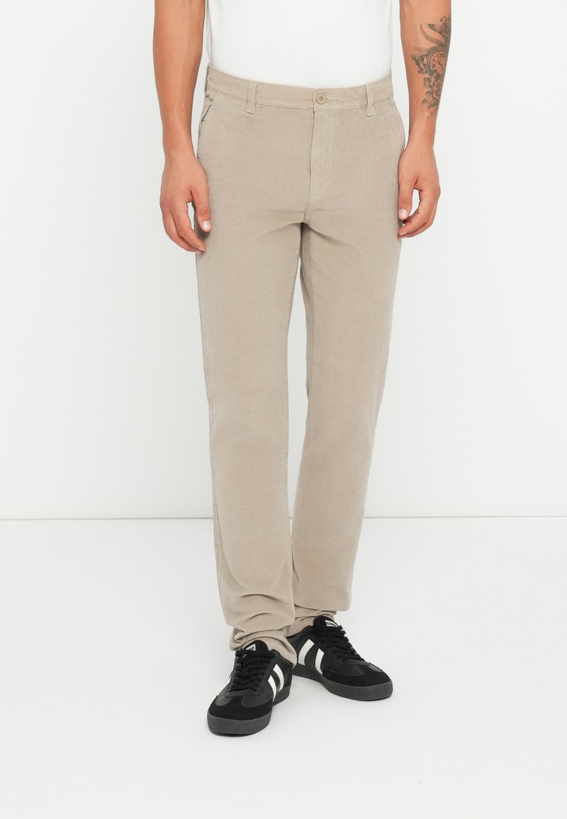 Chinos beige en coton avec des jambes droites, dotés de poches avant, d'une fermeture à bouton, portés avec des chaussures de sport noires.