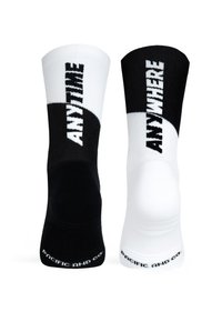 Černé a bílé ponožky s kontrastními polovkami. Každá strana nese text "KDYKOLIV" a "KDEKOLIV" v tučném, žebrovaném materiálu. Texturované podrážky.