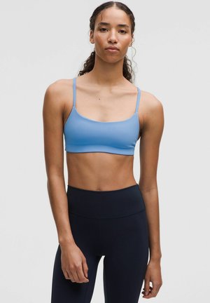 Light blue sport bra with thin straps, smooth texture, and a cropped design. Paired with high-waisted navy leggings.