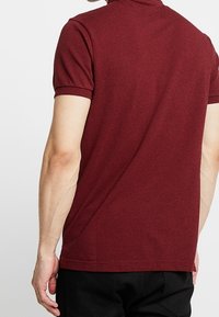 Burgundy kortärmad polo med mjuk textur, klassisk krage och subtila sömnadsdetaljer. Har en rak nederkant och figursydd silhuett.