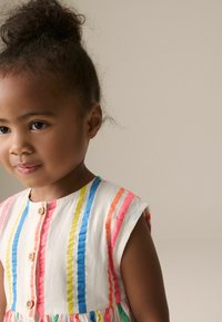 Robe en coton avec des rayures verticales colorées en rouge, bleu, jaune et vert. Avec des manches courtes et des boutons en bois sur le devant.