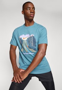 Camiseta de algodón azul cielo con un diseño gráfico que presenta un camino y follaje; texto "NO HAY LÍNEA DE META" en color rosa. Cuello redondo estándar.