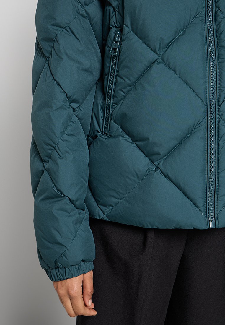 Turkusowa kurtka puchowa z diamentowym pikowaniem, zamykaną na zamek kieszenią na piersi oraz elastycznymi mankietami. Miękka, gładka struktura i lekka konstrukcja.