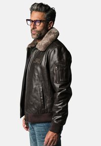 Veste aviateur en cuir marron avec un col en fausse fourrure, poches zippées et à pression, poignets et ourlet côtelés, avec un patch sur la poitrine.