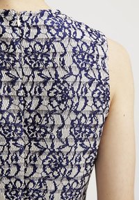 Spitzenkleid mit floralem Muster in Marineblau auf hellem Hintergrund. Verfügt über einen hohen Ausschnitt und einen verdeckten Reißverschluss hinten.