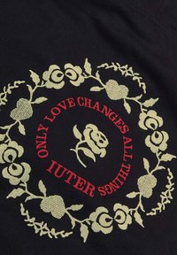 Tessuto nero con un motivo floreale in verde chiaro, che racchiude un testo rosso che recita "ONLY LOVE CHANGES ALL THINGS IUTER."