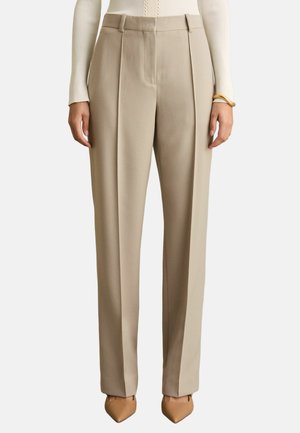 Pantaloni beige su misura a vita alta con piega frontale, abbinati a un top crema a coste maniche lunghe e scarpe color cammello con punta.