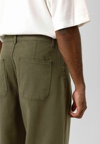 Groene katoenen broek met een rechte snit, voorzien van twee achterzakken en een gestructureerde stof. Zichtbare stiknaden op de tailleband.