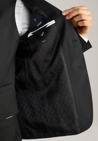 Schwarzer Blazer mit schlanker Passform. Das Innenfutter besteht aus einem glatten schwarzen Stoff mit einem dezenten Muster und enthält ein Etikett mit dem "JOOP!"-Logo.