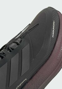 Černá atletická bota s texturovaným povrchem, zdobená třemi rýhovanými pruhy na boku a vínovou gumovou podrážkou s detaily značky.