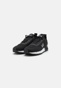 Zapatillas deportivas negras con parte superior de tejido, diseño elegante, suela blanca y marcas en los lados. Superficie texturizada para un mejor agarre.
