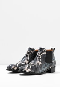 Botas de tobillo con estampado de serpiente que presentan una mezcla de colores negro, gris y crema. Textura suave con paneles laterales elásticos y un tac�ón bajo.