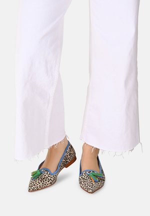 Leopardmønstrede flade sko med spidse tæer og grønne, blå og orange frynser; båret med slidte hvide vide bukser.
