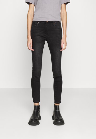 Černé skinny džíny z denimu, s středně vysokým pasem, pěti kapsami a hladkým povrchem. Spárovány s černými kotníkovými botami.