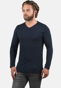Marineblauw lang mouws T-shirt met V-hals gemaakt van een gladde stof, met een aansluitend ontwerp en matige rek, gecombineerd met grijze spijkerbroeken.