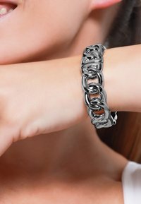 Bracciale in argento con anelli intrecciati, caratterizzato da una finitura lucida e un design leggermente curvato, indossato su un polso.