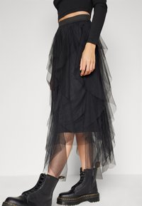 Black layered tulle skirt with a textured finish, featuring a fitted waistband. Paired with black lace-up ankle boots with chunky soles.