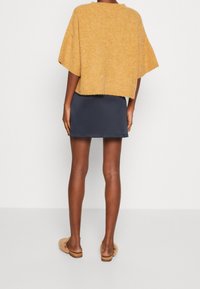 Senapsgul stickad kortärmad tröja, marinblå figurnära kjol och ljusbruna slidesandaler, sedd bakifrån.