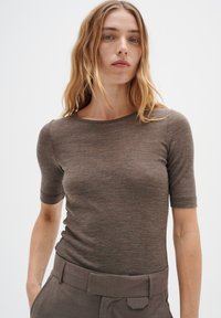 Hnedý krátky rukáv top vyrobený z jemného pleteného materiálu s okrúhlym výstrihom; model skombinoval s vysokými, upravenými šedými nohavicami.