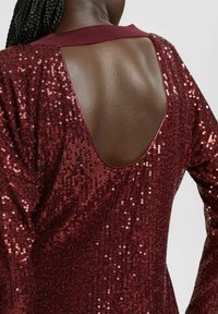 Burgundy paljettopp med djup V-rygg, med ribbad halsringning och mjuk textur, som visar glimmande paljetter över tyget.