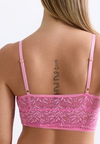 Roze kanten bralette met bloemenpatroon, verstelbare satijnen banden en gouden hardware accenten. Zacht, gestructureerd materiaal; middellange ontwerp.