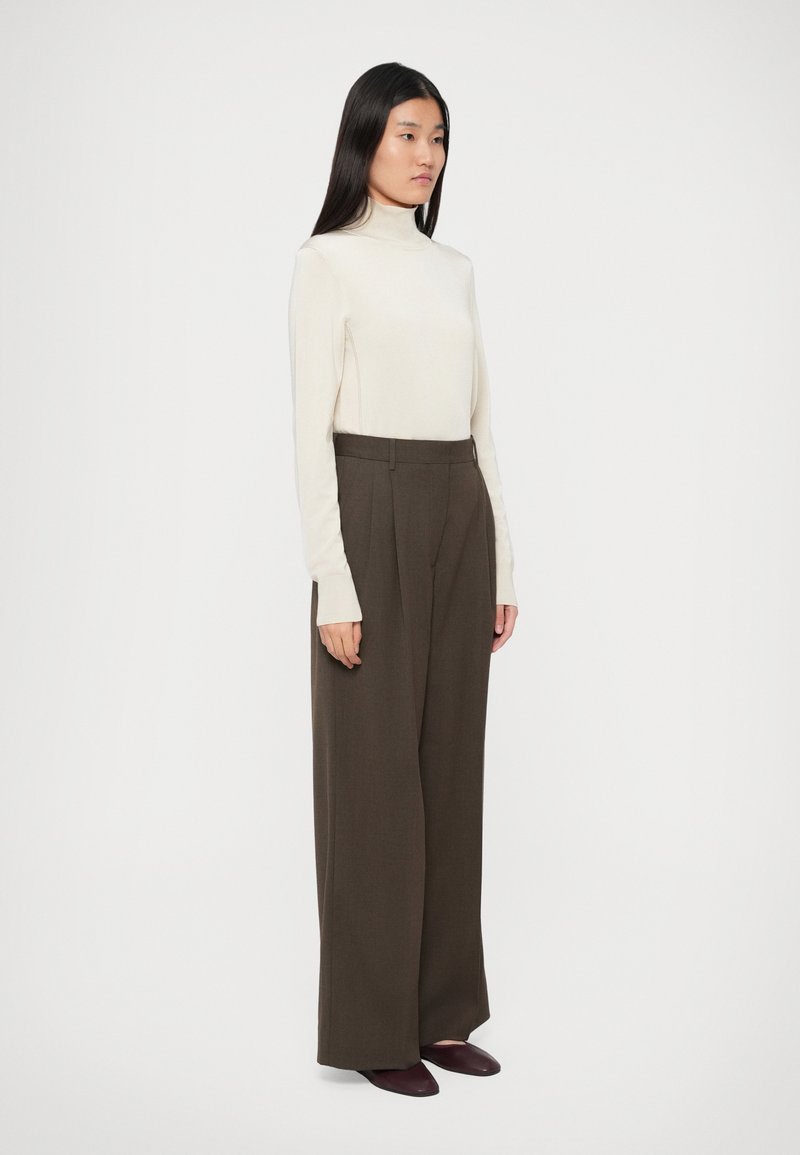 Cream turtleneck sweater paired with high-waisted, wide-leg brown trousers. Smooth texture with subtle tailoring; flat maroon shoes complete the look.