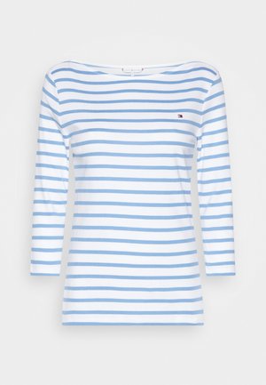 Hvid langærmet skjorte med lyseblå vandrette striber og et lille rødt, hvidt og blåt logo på venstre bryst.