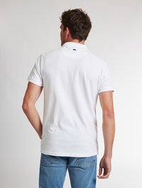 Bílá polokošile s krátkým rukávem, klasickým límcem, hladkým povrchem a malou značkovou etiketou na zadní straně. Nosit s modrými džínami.