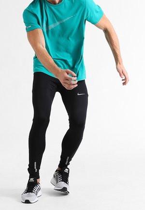Mann in türkisfarbenem Sportshirt und schwarzen Leggings mit Nike-Logo, der sich nach vorne streckt, trägt schwarze und weiße Nike-Laufschuhe.