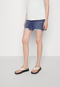 Denim mini-hame, jossa on revitty helma, slim-fit -mallilla ja vaaleansinisen pesun värillä. Yhdistettynä beigellä flip-flop -sandaaleilla mustilla alustalla.