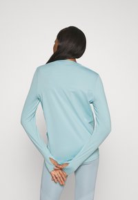 Hellblaues Langarmoberteil mit gerippter Textur und Daumenlöchern, kombiniert mit passenden hellblauen Leggings. Rückansicht, glattes Design.