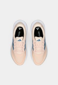 Gaiši rozā sporta apavi ar zilām svītrām, tīkliņa augšdaļa un baltas zolītes. Iespējas ietver mīkstinātu Ortholite zolīti un plakanas auklas.