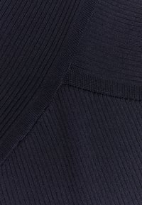 Skręcony dzianinowy materiał w ciemnym granacie, z różnymi fakturami, gładkim wykończeniem oraz subtelnymi akcentami na powierzchni.