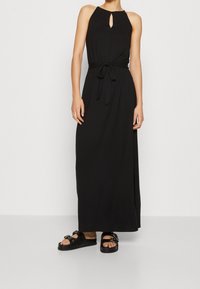 Svart maxiklänning med halterneck och nyckelhålsdetalj, åtsittande i midjan med ett band, i kombination med svarta sandaler utan klack med metalliska detaljer.