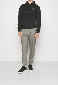 Svart hoodie med ficka fram och logotyp, tillsammans med grå rutiga byxor och svarta sneakers med vita sulor. Avslappnad outfit.